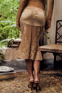 Person wearing a beige lace skirt in an indoor setting with plants and a chair.