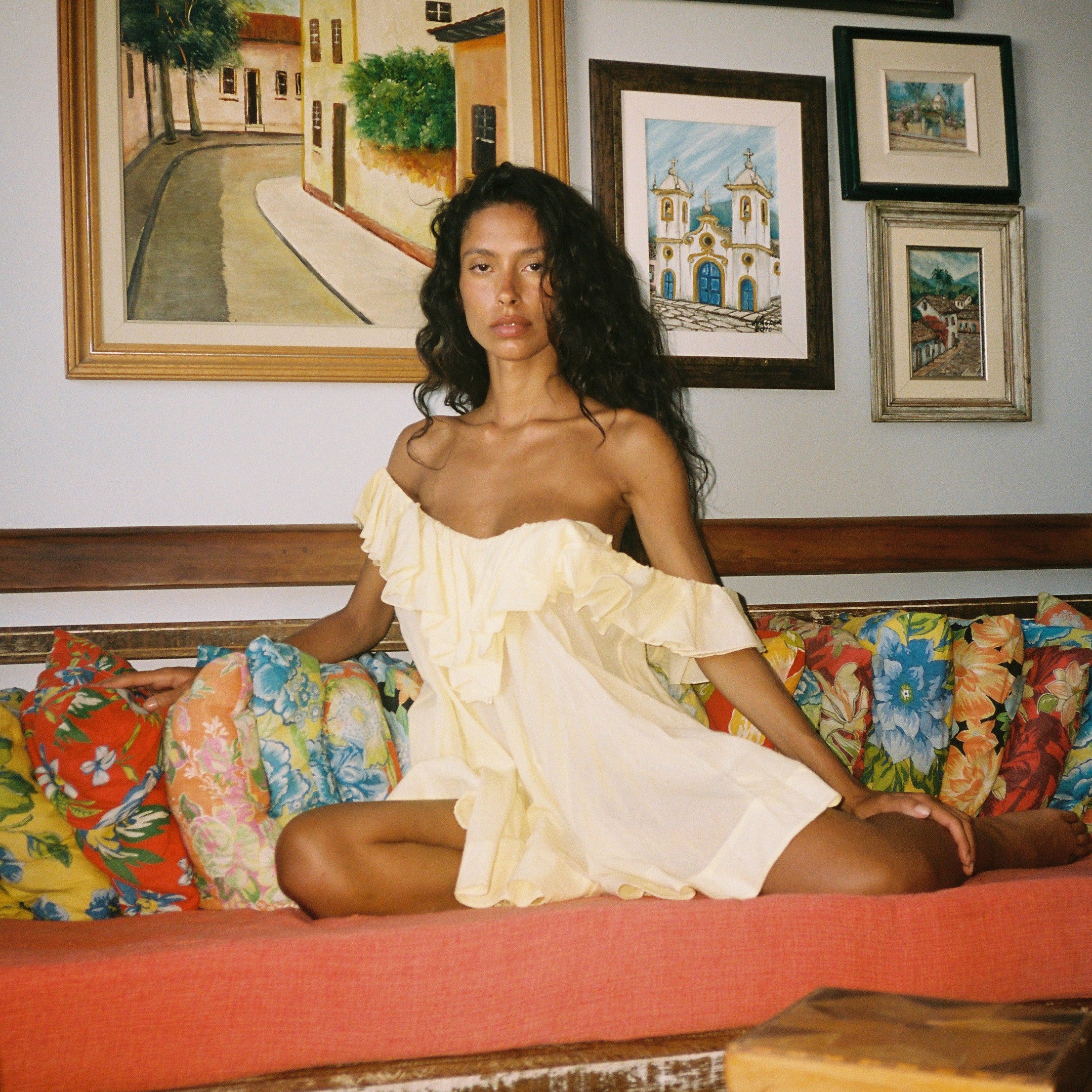 Woman in a white dress sitting on a colorful couch with framed artwork in the background