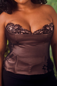 Fishnet and satin corset top with lace detailing on a blurred green background